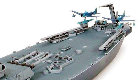 A detailed miniature model of an aircraft carrier deck with two blue and white fighter jets on a white background.